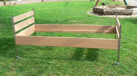 Ein Bett aus gebürstetem Edelstahl und Buchenholz steht auf dem Rasen