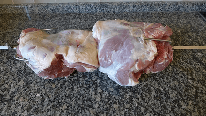 Zwei rohe Lammkeulen liegen auf einem Spieß auf der Arbeitsplatte