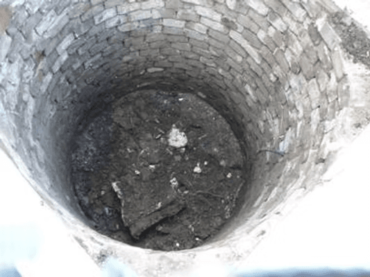 Blick von oben in den gemauerten Brunnenschacht, der mit Müll verfüllt ist