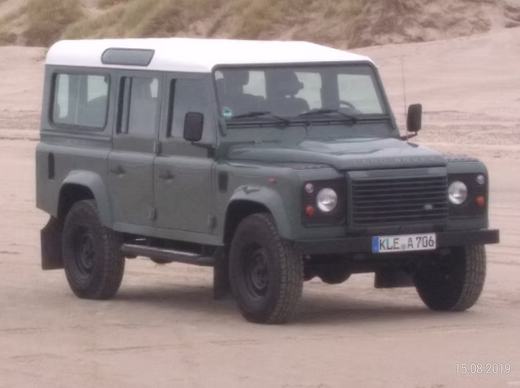 Der Defender in Keswick Green mit weißem Dach auf sandigem Boden