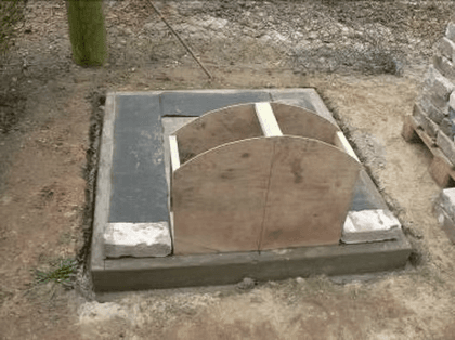 Eine halbrunde Sperrholzschablone und die ersten Feldbrandsteine auf dem Fundament