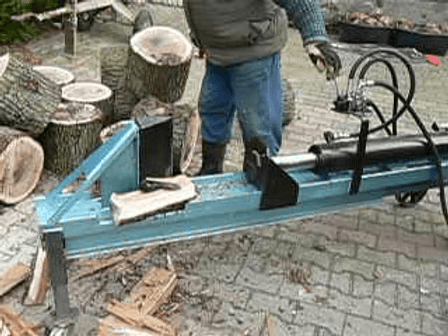 Der blau lackierte Holzspalter im Einsatz, daneben gespaltene Holzklötze