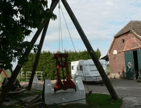 Ein Dreibein aus Strommasten steht über dem Brunnen, daran hängt der rote Seilgreifer