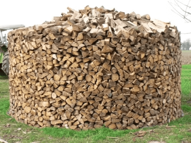 Eine runde, sorgfältig aufgeschichtete Holzmiete auf der Wiese