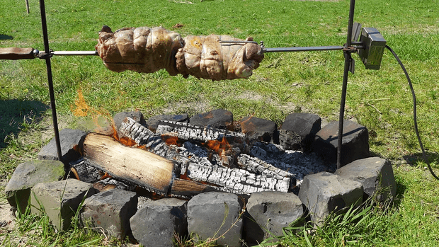 Zwei Lammkeulen drehen sich am Spieß über einem offenen Feuer im Garten