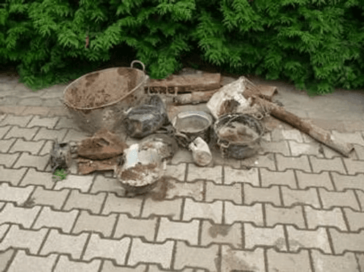 Fundstücke aus dem Brunnen auf dem Pflaster: alte Eimer, Töpfe und Metallteile