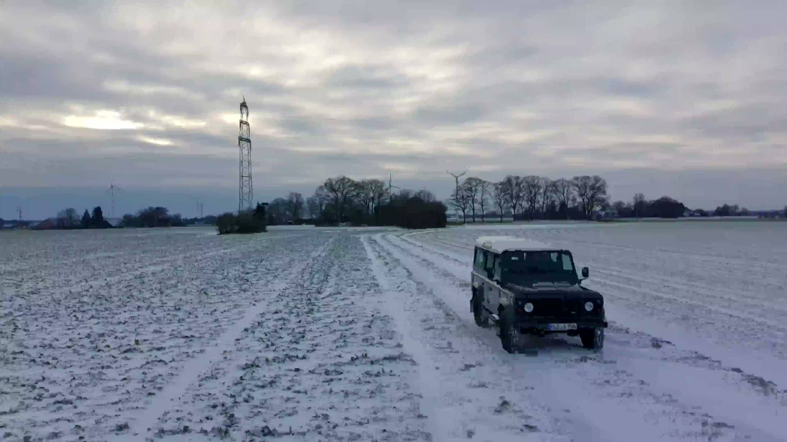 Der grüne Land Rover Defender mit weißem Dach fährt auf einem verschneiten Feldweg auf die Kamera zu